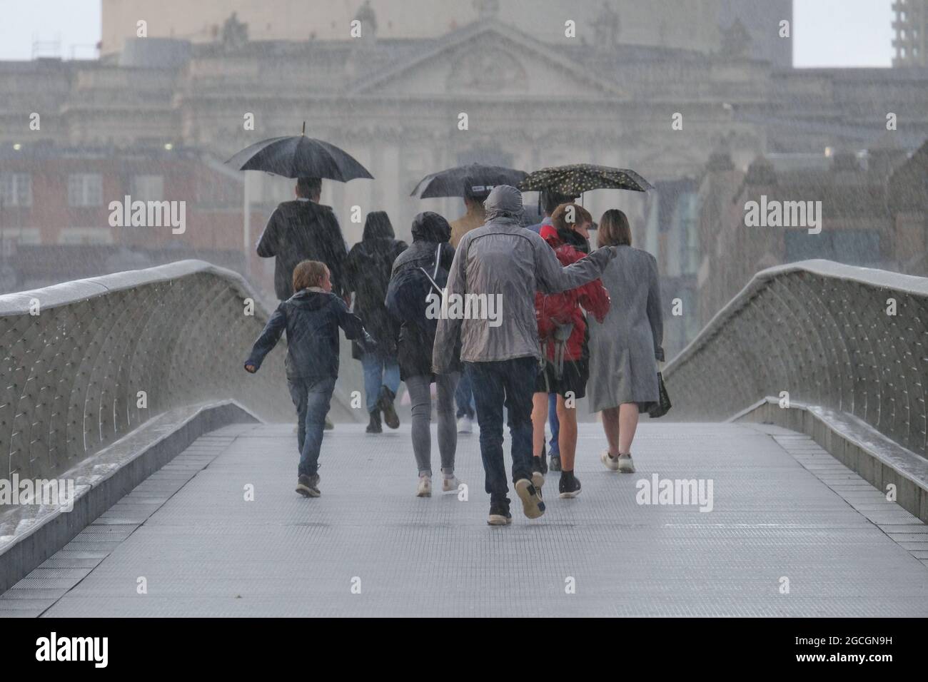 Londra, Regno Unito. Un gruppo di persone cammina lungo il Millennium Bridge durante una discesa torrenziale. Recenti forti piogge hanno causato un'inondazione di flash. Foto Stock