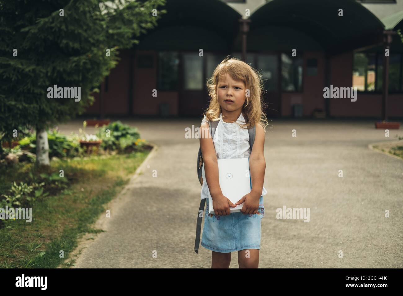 La ragazza seria, studente di scuola elementare, a piedi a scuola con borsa dietro e libro. Gli studenti sono pronti per il nuovo anno. Ritorno a scuola. Foto Stock