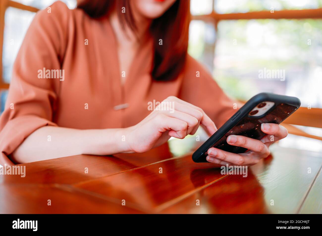 Primo piano di una giovane bella donna che sta testando e sfogliando app e social media sullo smartphone mentre si siede in un moderno cafe in attesa di caffè Foto Stock
