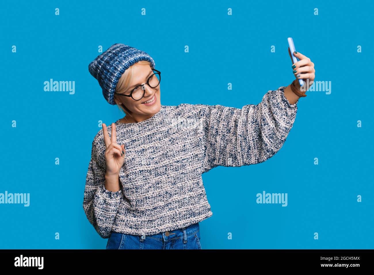 Immagine elegante con donna in maglia cappello che fa selfie. Look alla moda. Gesto di pace. Foto Stock