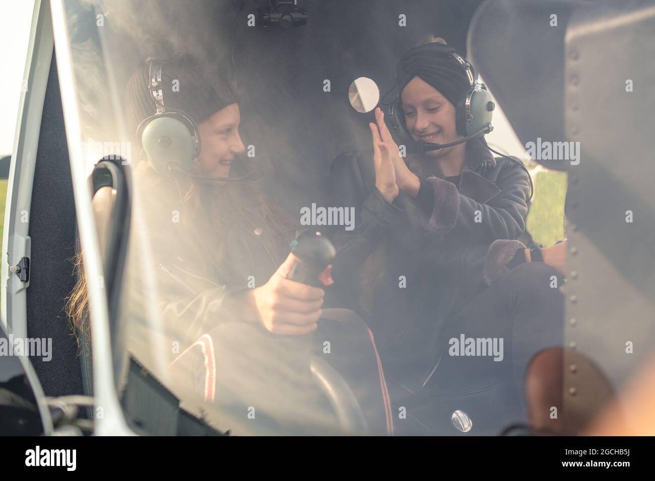 Sorridendo le ragazze adolescenti in cuffie pilota che danno alto cinque in elicottero Foto Stock