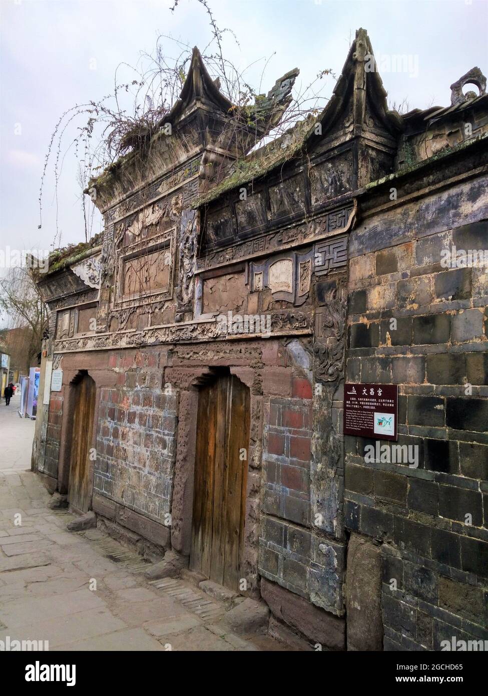 Un antico edificio nel quartiere di Lizhuang con vecchie mura, porte in legno e mattoni coltivati con piante e felci. Foto Stock