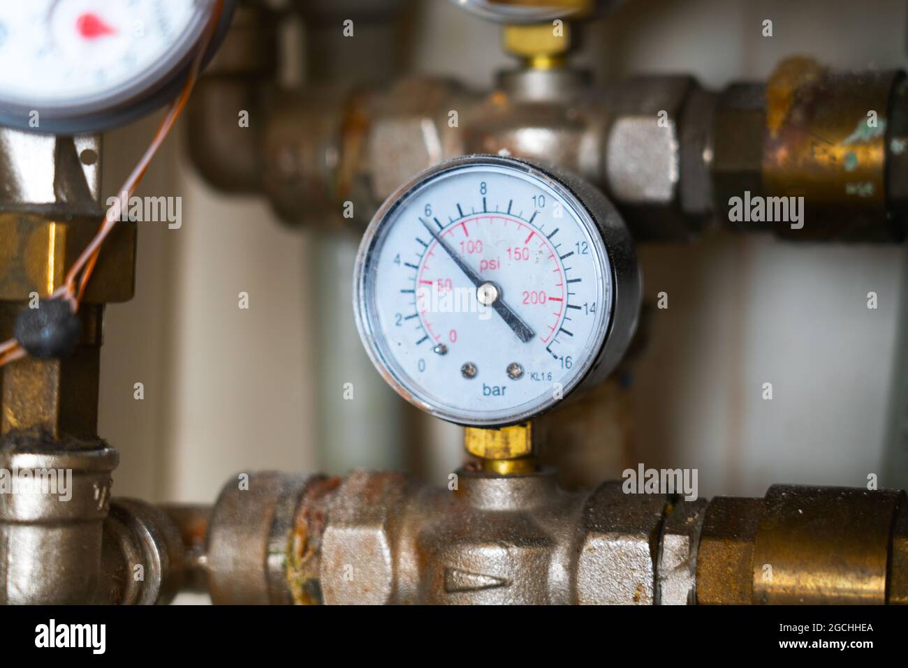 Sistema di tubazioni complesso con manometro analogico caldo con polvere, sporco, macchie sporche. Collettore dell'acqua con manometro e valvola di controllo della pressione. Foto Stock