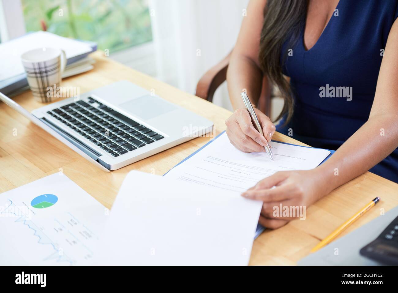 Donna d'affari che lavora con i rapporti, rispondendo alle e-mail e firmando gli accordi al suo tavolo d'ufficio Foto Stock