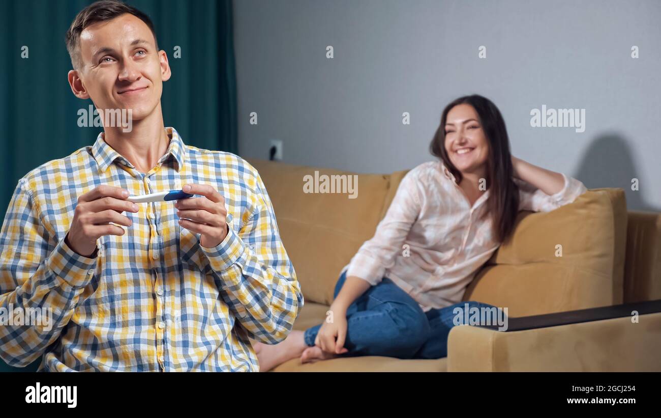 Il giovane caucasico guarda indietro alla sua felice moglie incinta. La gioia della paternità imminente Foto Stock