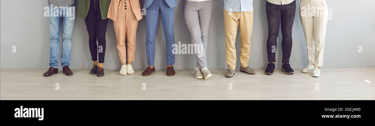 Immagine ritagliata di gambe di persone in piedi in una fila vicino al muro in attesa di un colloquio. Foto Stock