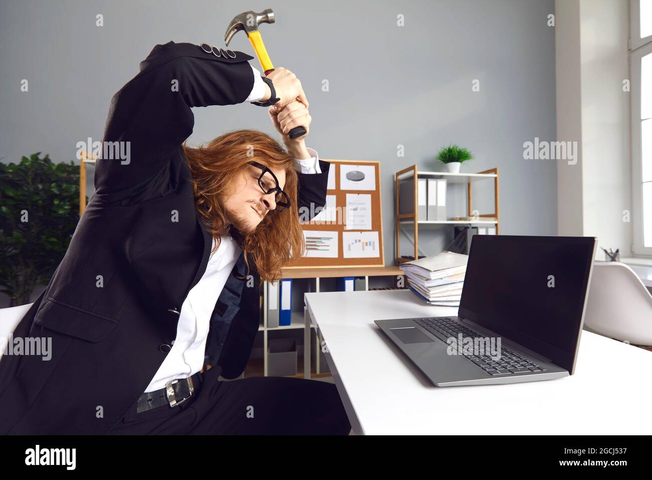 Arrabbiato stressato lavoratore in ufficio che ha colpito il computer portatile con martello in cattive giornate di lavoro Foto Stock