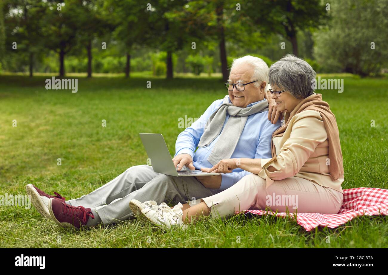 Felice coppia senior che usa un computer portatile mentre si siede su un prato insieme Foto Stock