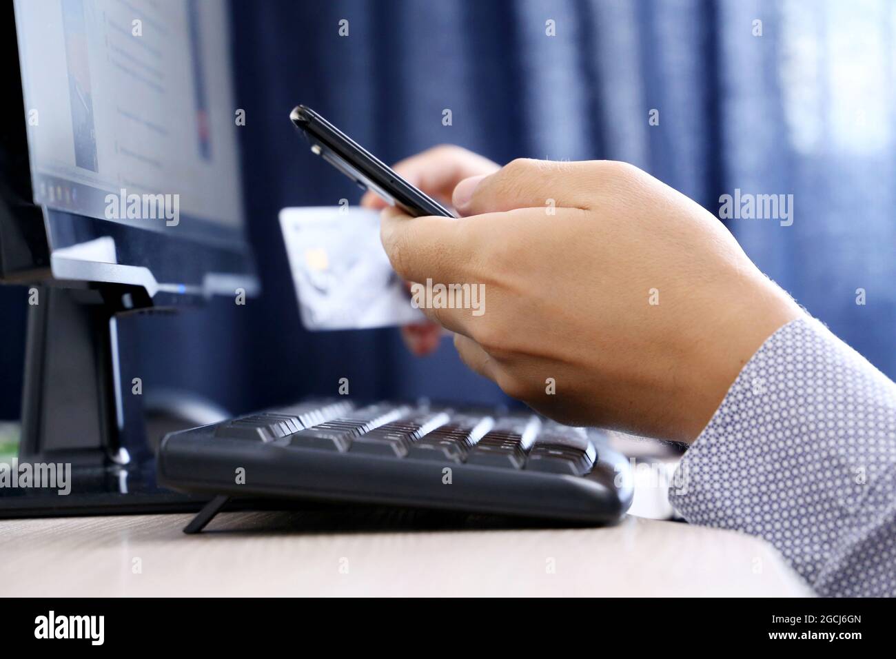 L'uomo tiene lo smartphone e la tastiera della carta di credito sulla tastiera del PC. Concetto di acquisto e pagamento online, transazioni finanziarie Foto Stock