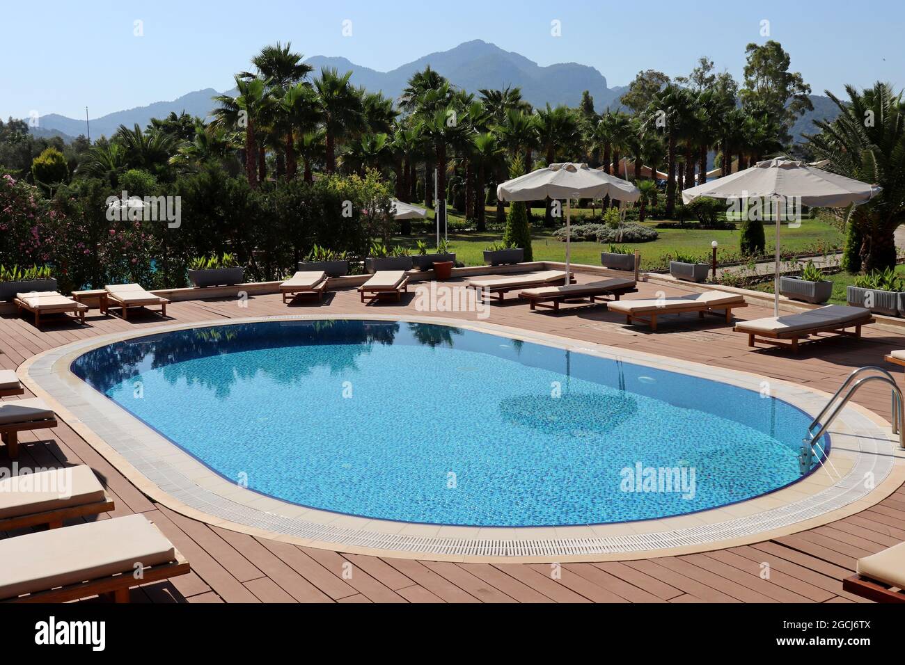 Vista sulla piscina vuota, sulle sdraio e sugli ombrelloni in un giardino con palme. Vacanza in un resort tropicale sullo sfondo delle montagne Foto Stock