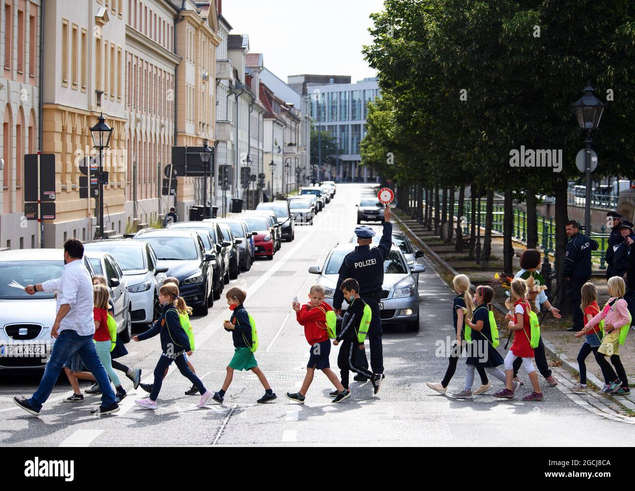 09 agosto 2021, Brandeburgo, Potsdam: Il sovrintendente della polizia Tezlaff ferma le auto sul Yorckstraße, che è designato per la velocità 30, alla scuola elementare Max Dortu in modo che i bambini della classe 2a possano attraversare la strada. Nei primi quaranta giorni dopo l'inizio della scuola dopo le vacanze estive, la polizia ha in programma di aumentare il controllo del traffico in tempi prioritari. Allo stesso tempo, la campagna di sicurezza stradale 'Lieber sicher. Lieber leben.' è stato lanciato per promuovere la considerazione tra ciclisti e autisti e per educare bambini e genitori sulla sicurezza stradale. Foto: Soeren Stache/dpa-Zentralbild/dpa Foto Stock