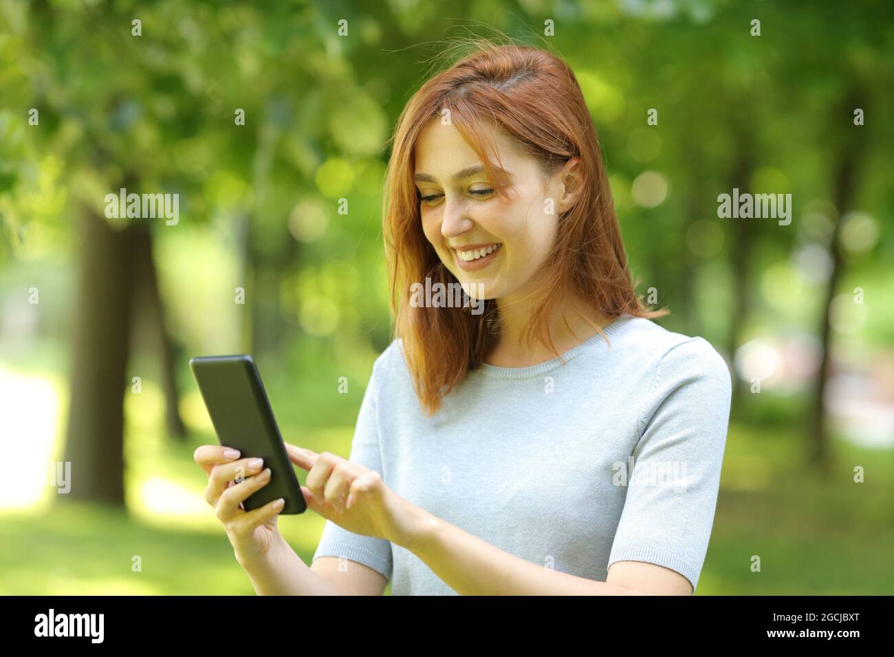 Felice donna utilizzando smartphone checkig online contenuti camminare in un parco Foto Stock