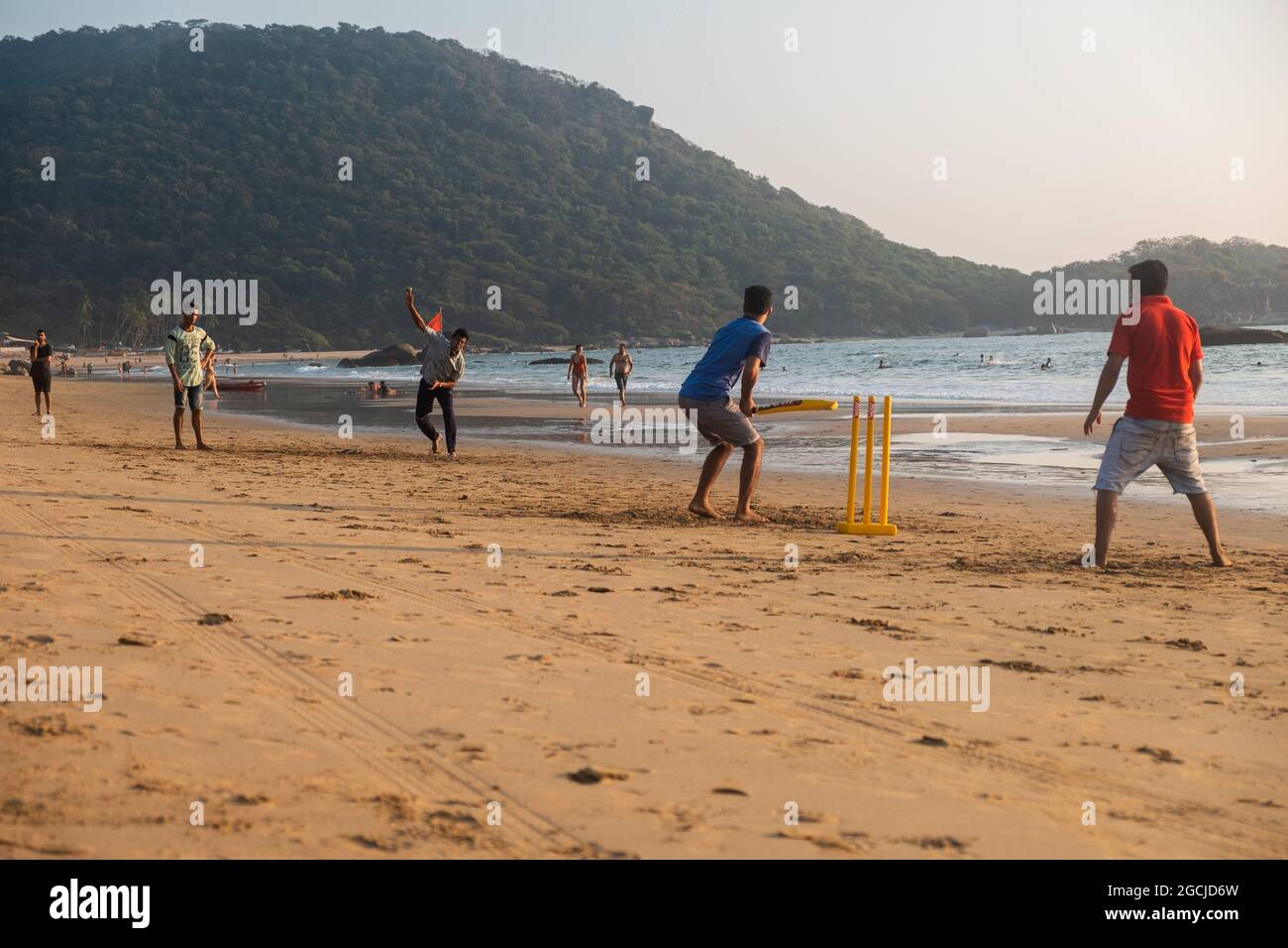 Gruppo di adulti indiani che giocano a cricket sulla spiaggia al tramonto, Goa, India Foto Stock