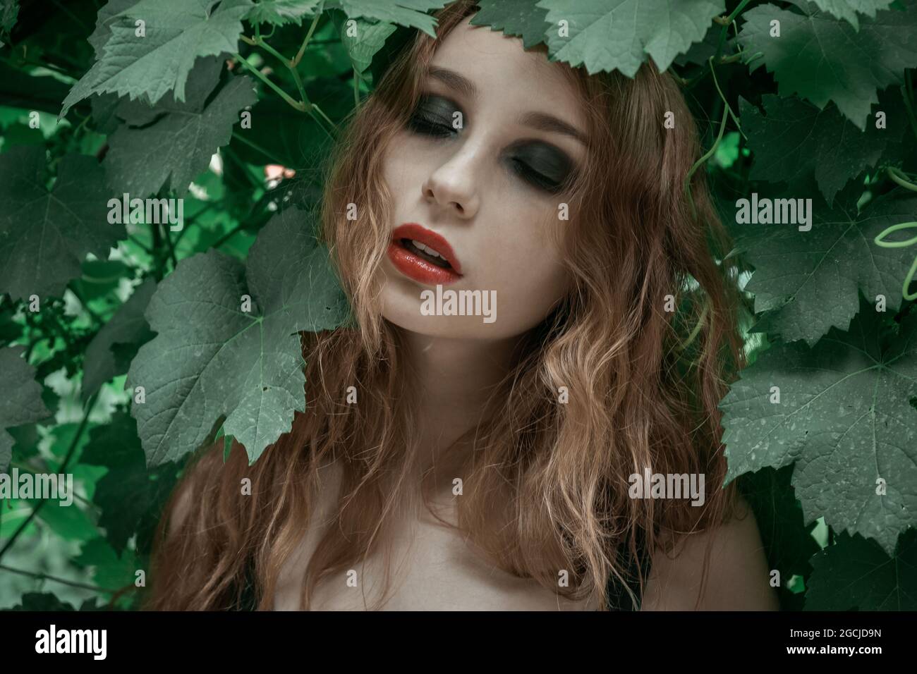 Ritratto di bella giovane donna con labbra rosse che rimangono davanti alle foglie verdi Foto Stock