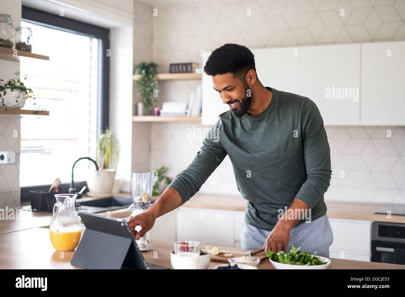 Giovane uomo con tablet preparare una sana colazione all'interno a casa, concetto di home Office. Foto Stock