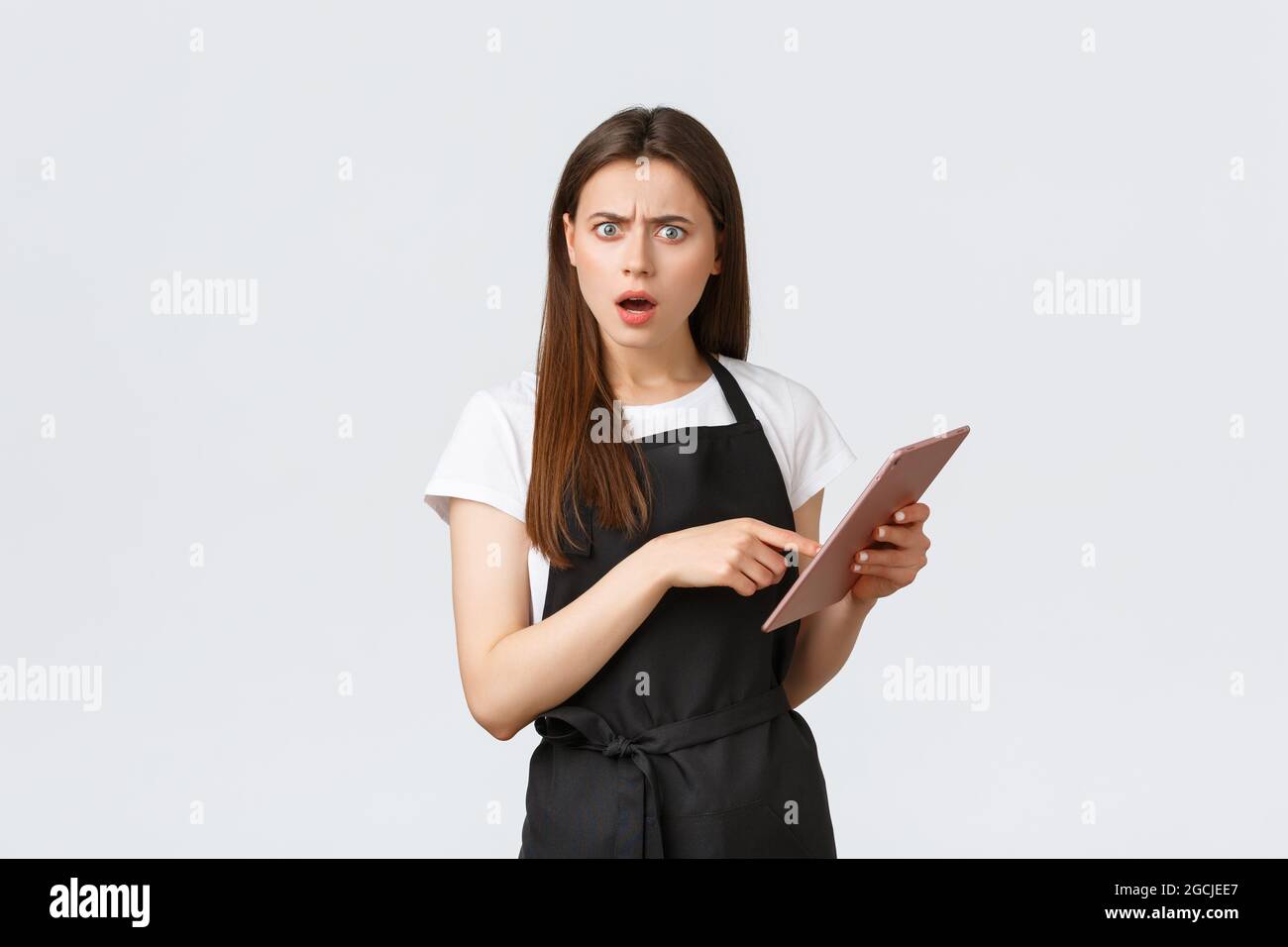 Dipendenti di negozi di alimentari, piccole aziende e caffè concetto. Cameriera femminile o lavoratore di caffè confuso e deluso che punta al tablet digitale Foto Stock