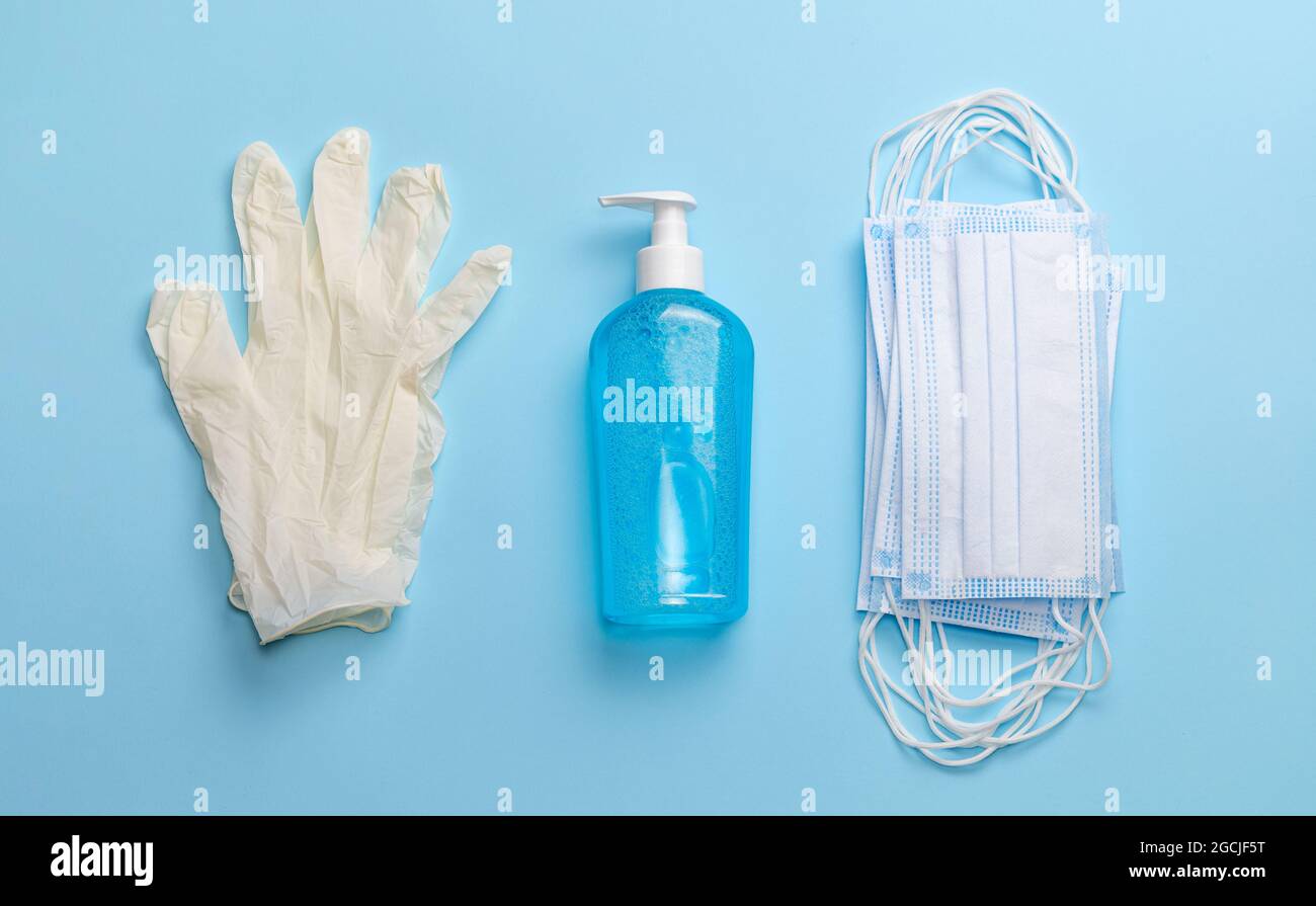 Guanti in lattice, disinfettante per le mani e maschere mediche su sfondo blu. Vista dall'alto. Foto Stock