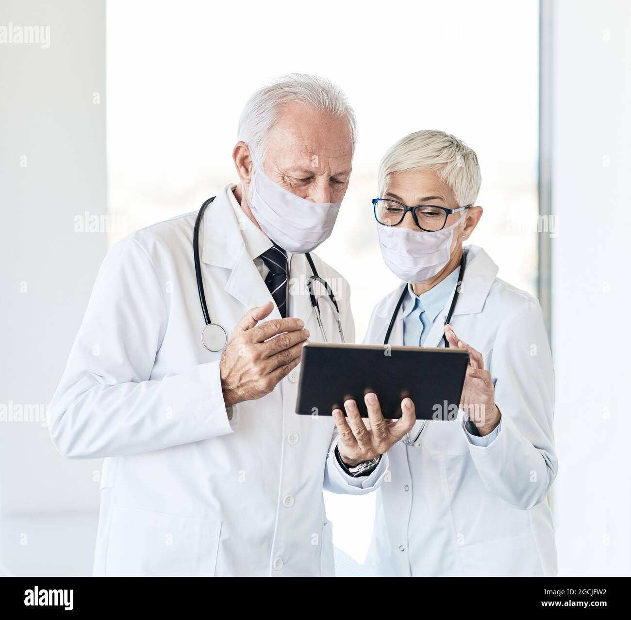 dottore senior conversazione ospedale sanità medicina tablet maschera virus protezione epidemia donna uomo Foto Stock