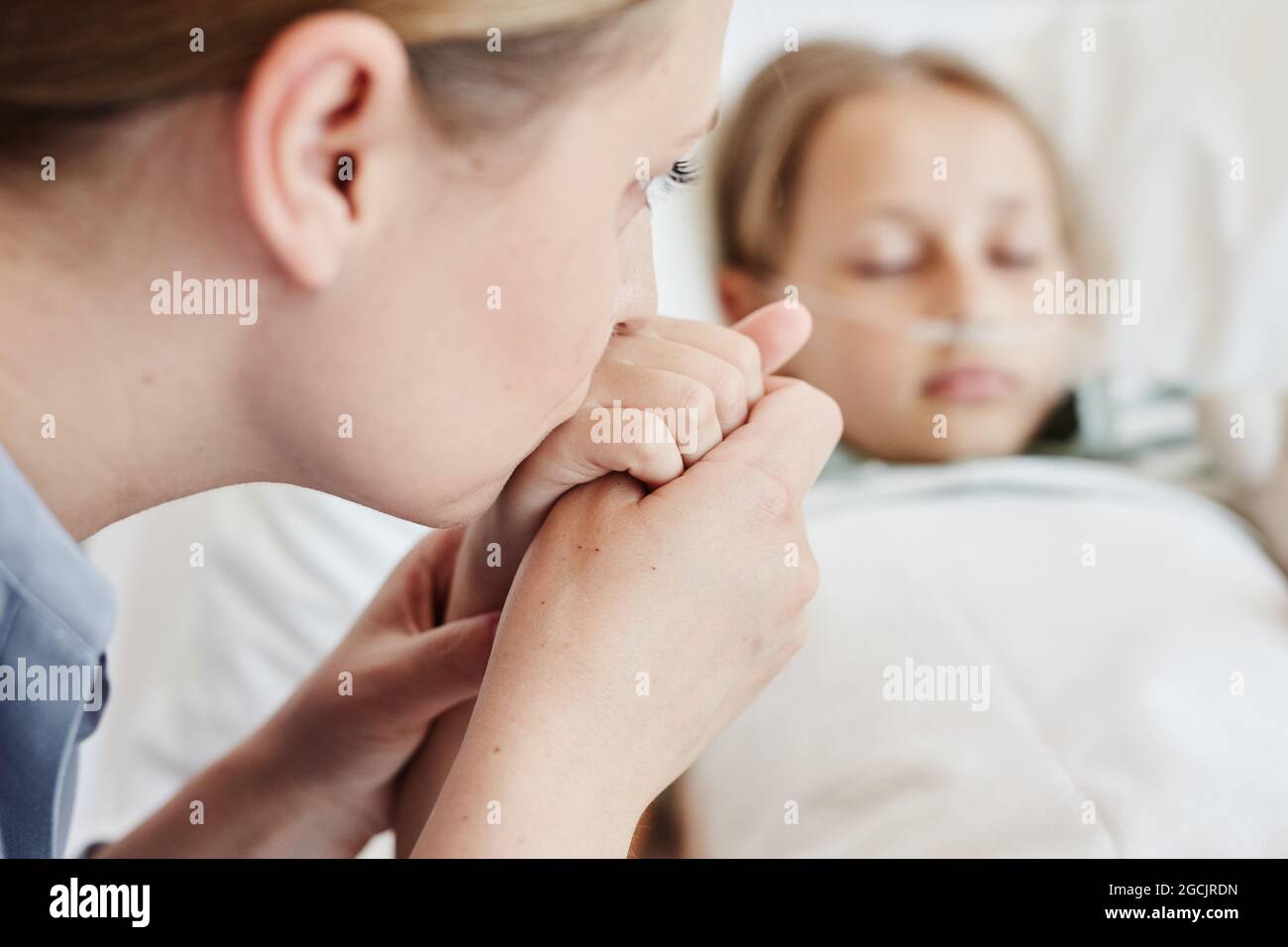 Primo piano di madre che tiene la mano del bambino malato nella stanza dell'ospedale con il supporto dell'ossigeno Foto Stock