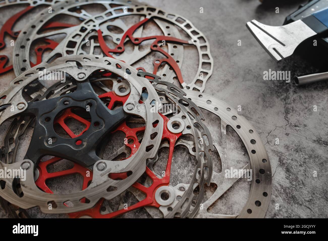 Dischi dei freni per mountain bike usurati giacenti in officina accanto all'attrezzo di raddrizzatura dei dischi. Foto Stock