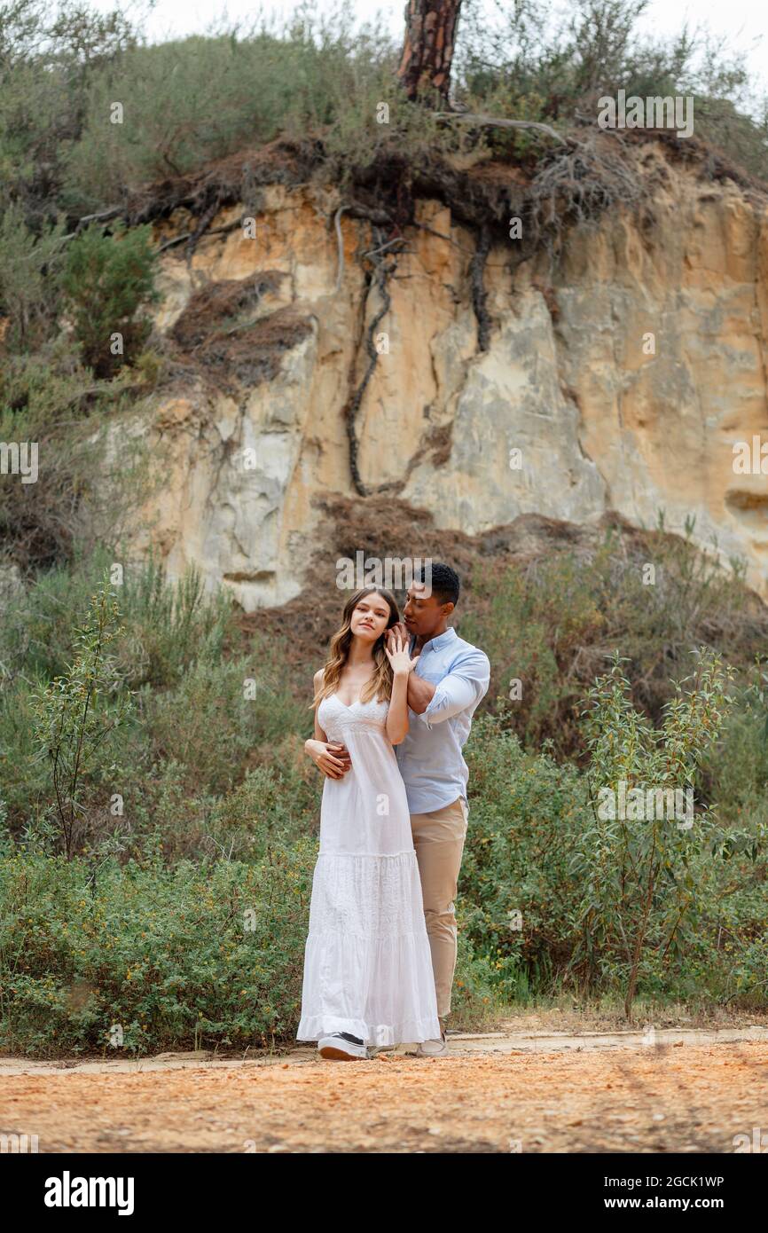 Felice sposa e sposo diversi abbracciando mentre si levano in piedi nella foresta il giorno del matrimonio Foto Stock