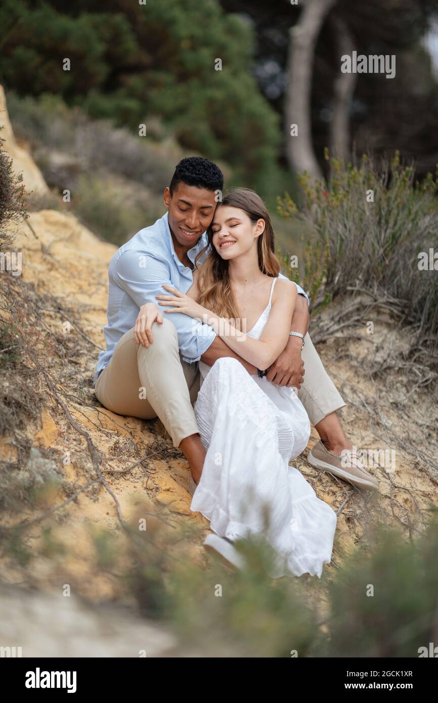 Soddisfare la coppia multirazziale degli sposi che si siedono in legno e abbracciano il giorno di nozze Foto Stock