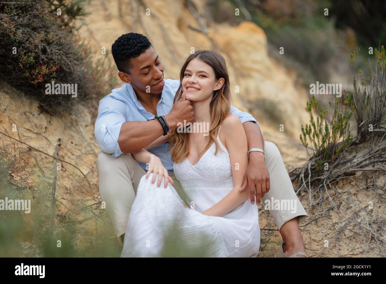Soddisfare la coppia multirazziale degli sposi che si siedono in legno e abbracciano il giorno di nozze Foto Stock