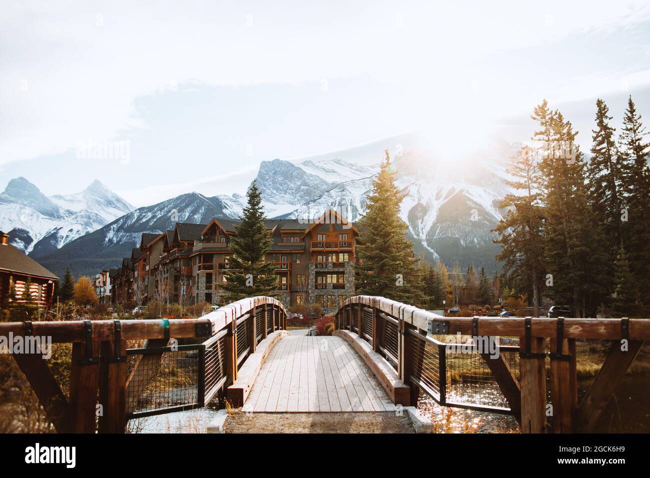 Pittoresco paesaggio autunnale con ponte e case di legno situato vicino al fiume contro le montagne innevate nella città di Canmore vicino al Parco Nazionale di Banff Foto Stock