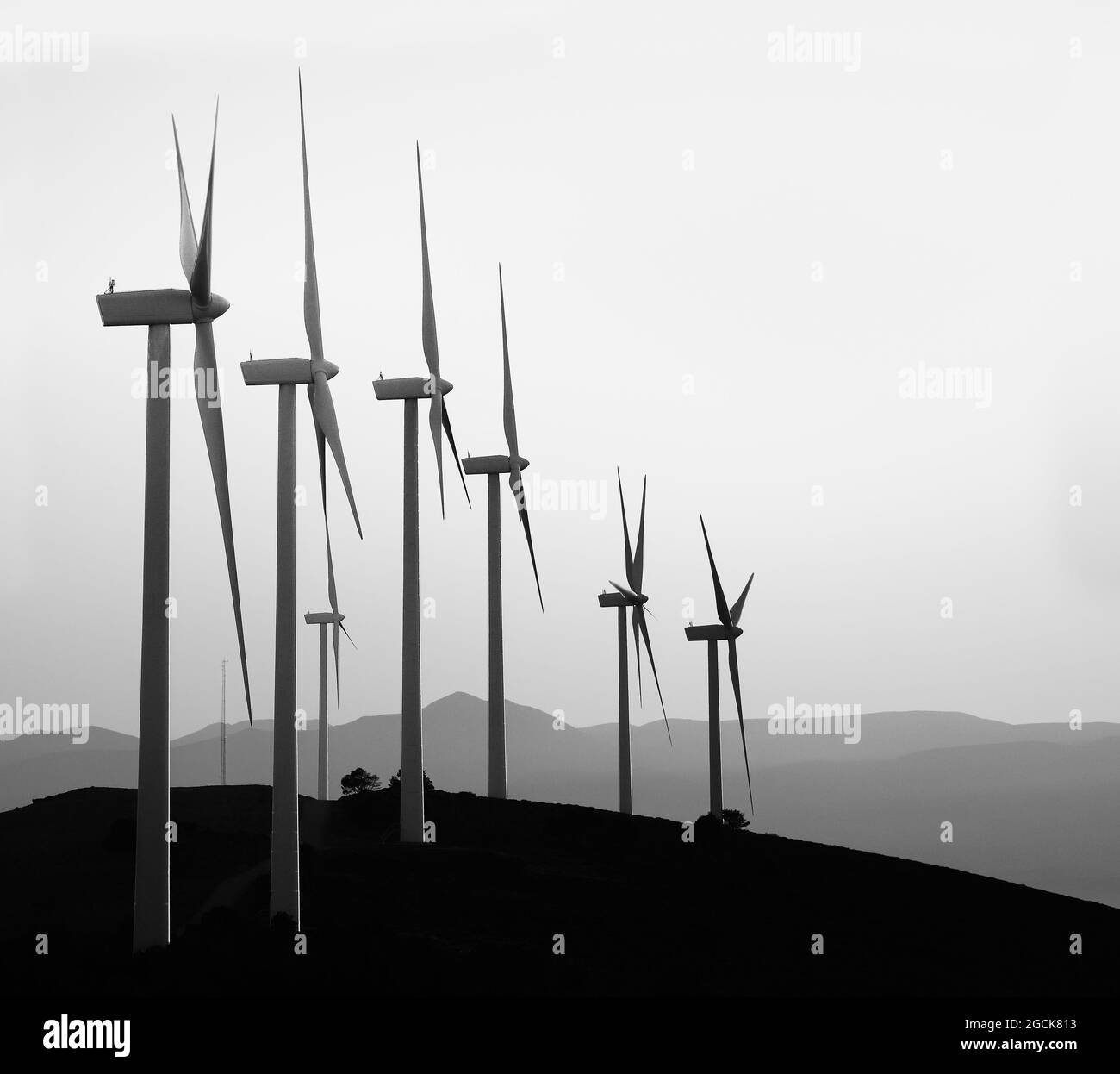 Mulini a vento contemporanei in bianco e nero posti in fila su una collina sullo sfondo della catena montuosa Foto Stock