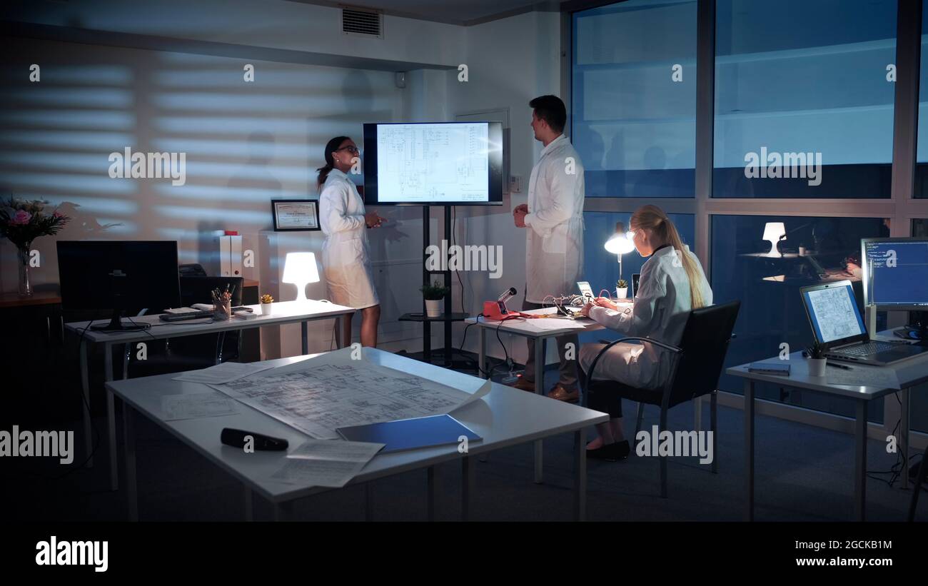 Team di ingegneri Informatici che discutono qualcosa su un grande schermo TV in laboratorio. Spiegano i dettagli della ricerca Foto Stock