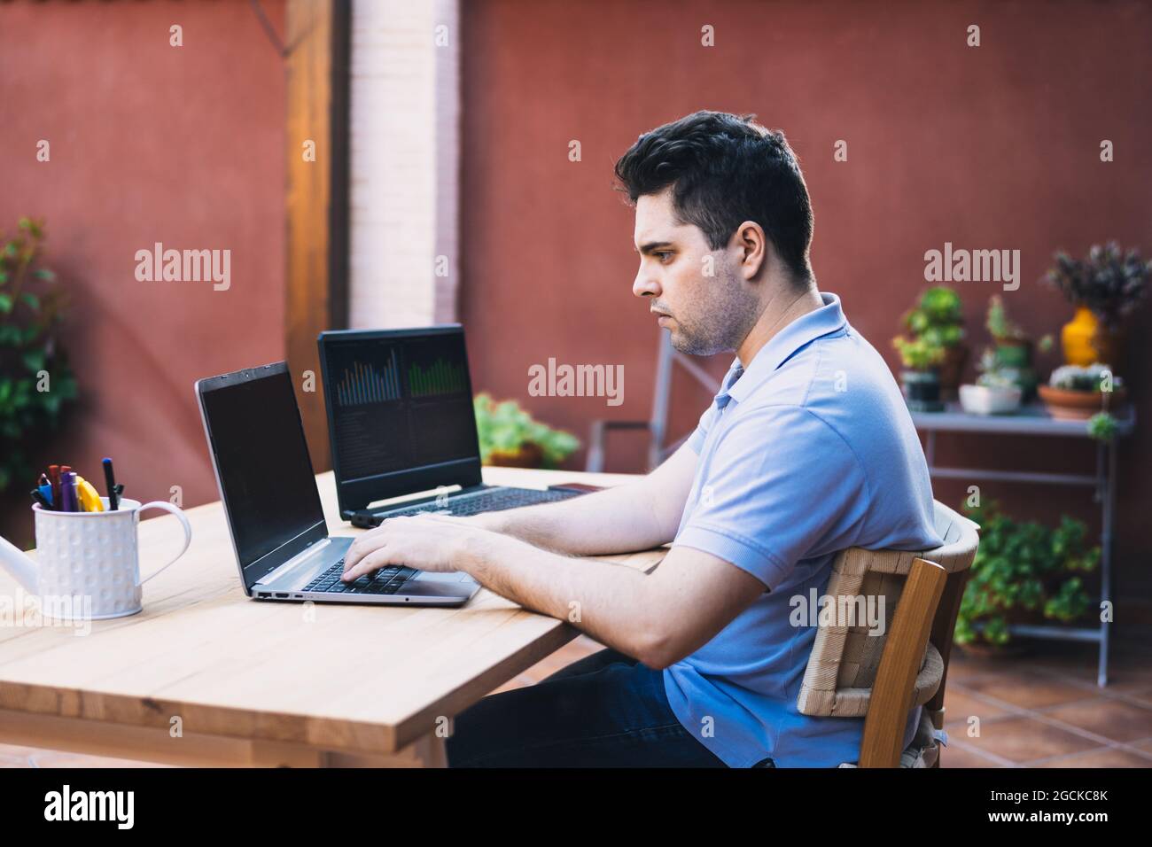 uomo seduto su una terrazza giardino utilizzando due computer portatili per il commercio di criptovalute Foto Stock