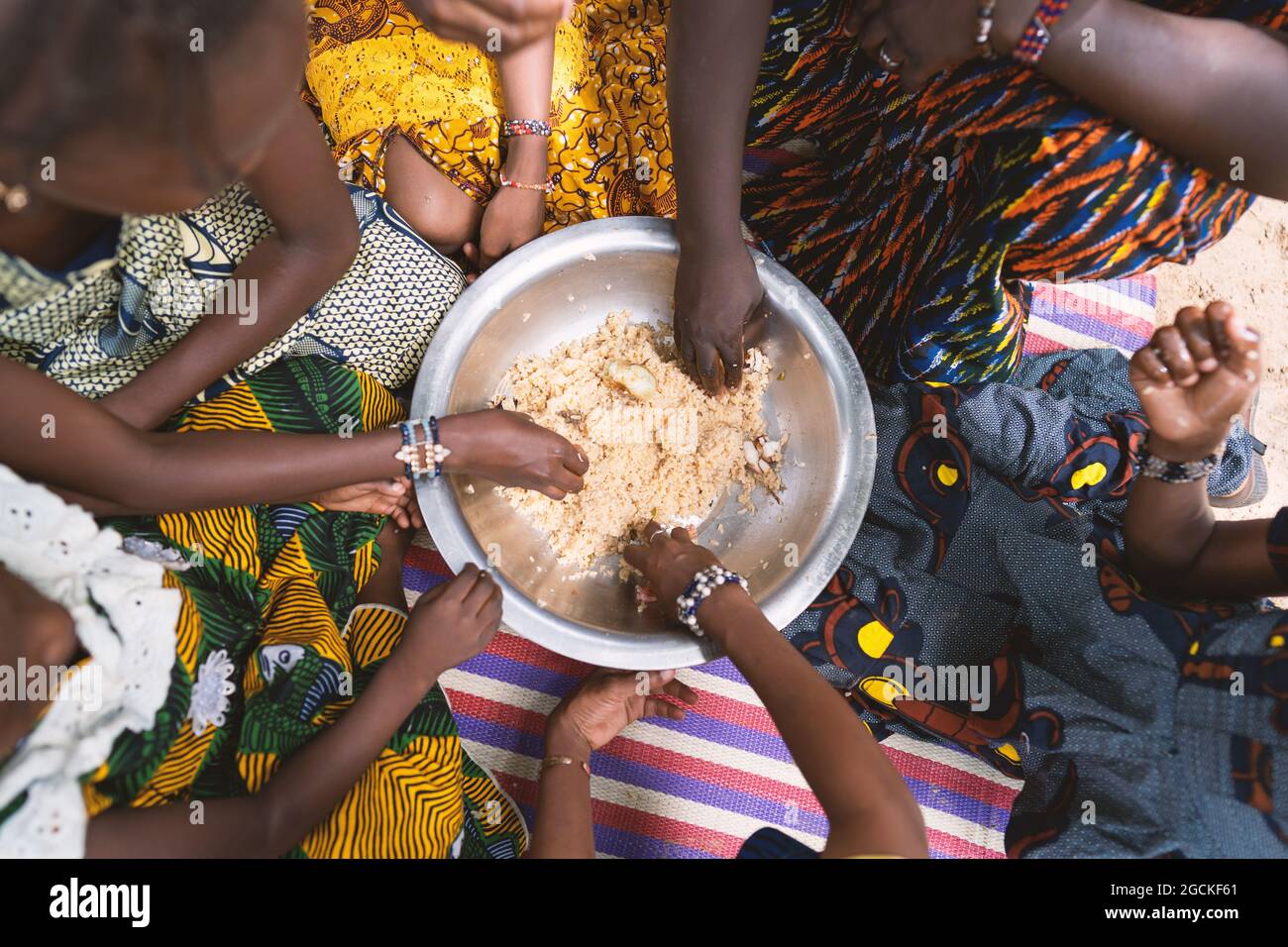 In questa immagine, un gruppo di ragazze africane nere è seduto in un cerchio intorno ad un grande piatto di cereali, mangiando il loro pasto vegan magro insieme con Foto Stock