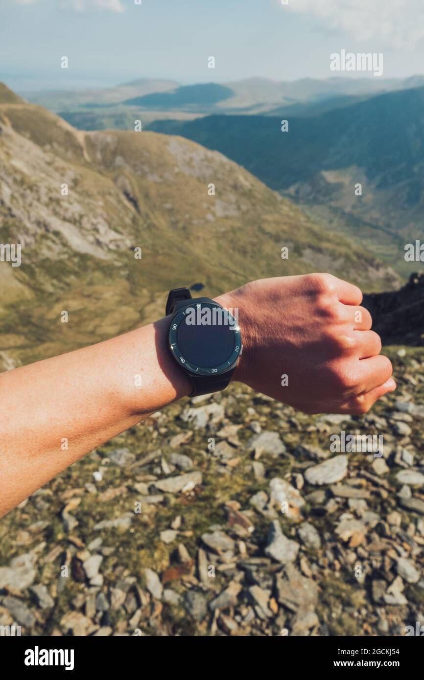 Cimentati con un ignoto escursionista che controlla il tempo sul smartwatch durante il trekking nelle alture durante il giorno di sole in Galles Foto Stock