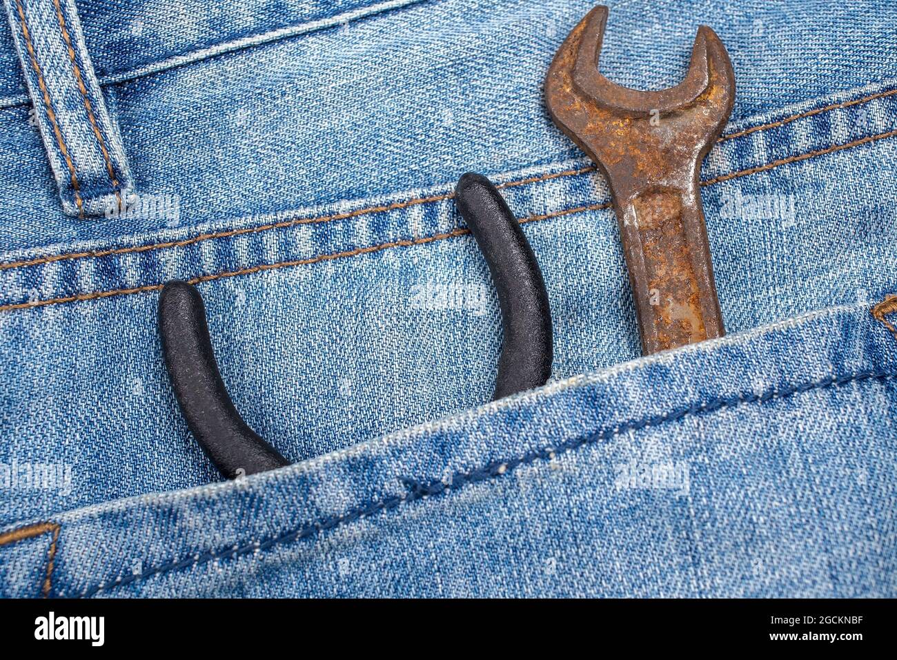 La chiave arrugginita e le pinze si trovano nella tasca posteriore dei jeans. Attrezzo in indumenti da lavoro speciali. Primo piano. Foto Stock