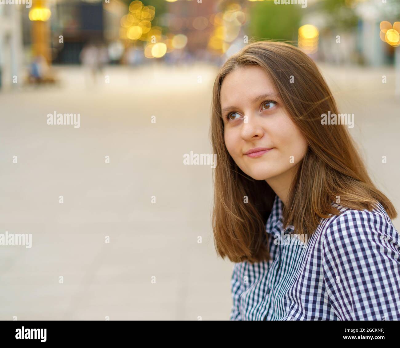 Ritratto di bella giovane donna con lunghi capelli biondi che guardano lontano contro la vista della città Foto Stock