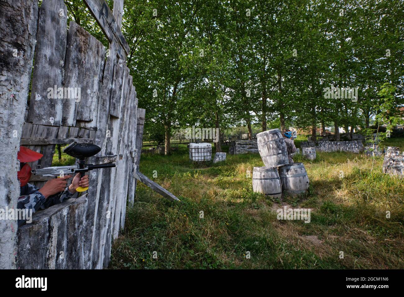 Sparatutto maschile anonimo con pistola paintball che mira a nemico nascondersi dietro barile di legno durante il gioco Foto Stock