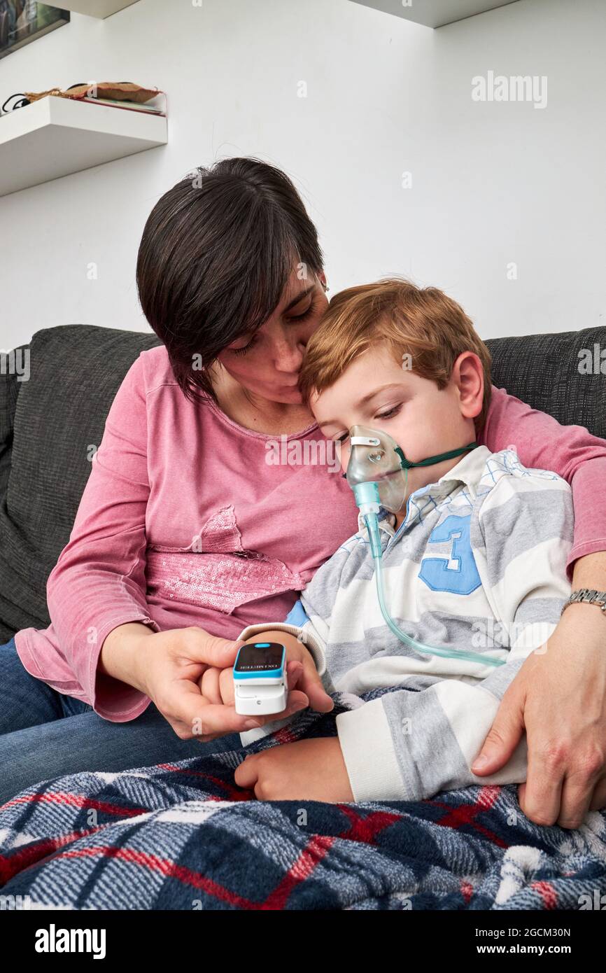 Donna che si prende cura di usare il pulsossimetro sul dito di un bambino malato in maschera di ossigeno usando il nebulizzatore durante l'inalazione a casa Foto Stock
