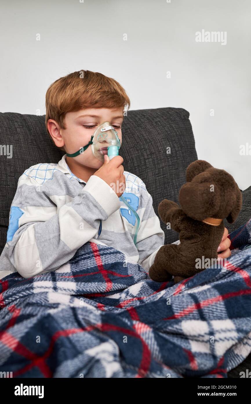 Bambino allegro che respira in maschera di ossigeno durante l'inalazione e  giocare con giocattolo morbido sul divano a casa Foto stock - Alamy