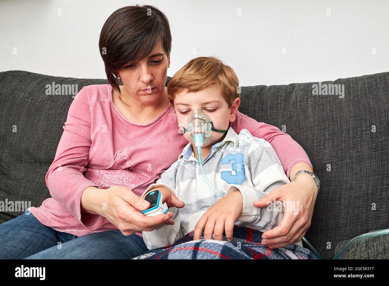 Donna che si prende cura di usare il pulsossimetro sul dito di un bambino malato in maschera di ossigeno usando il nebulizzatore durante l'inalazione a casa Foto Stock