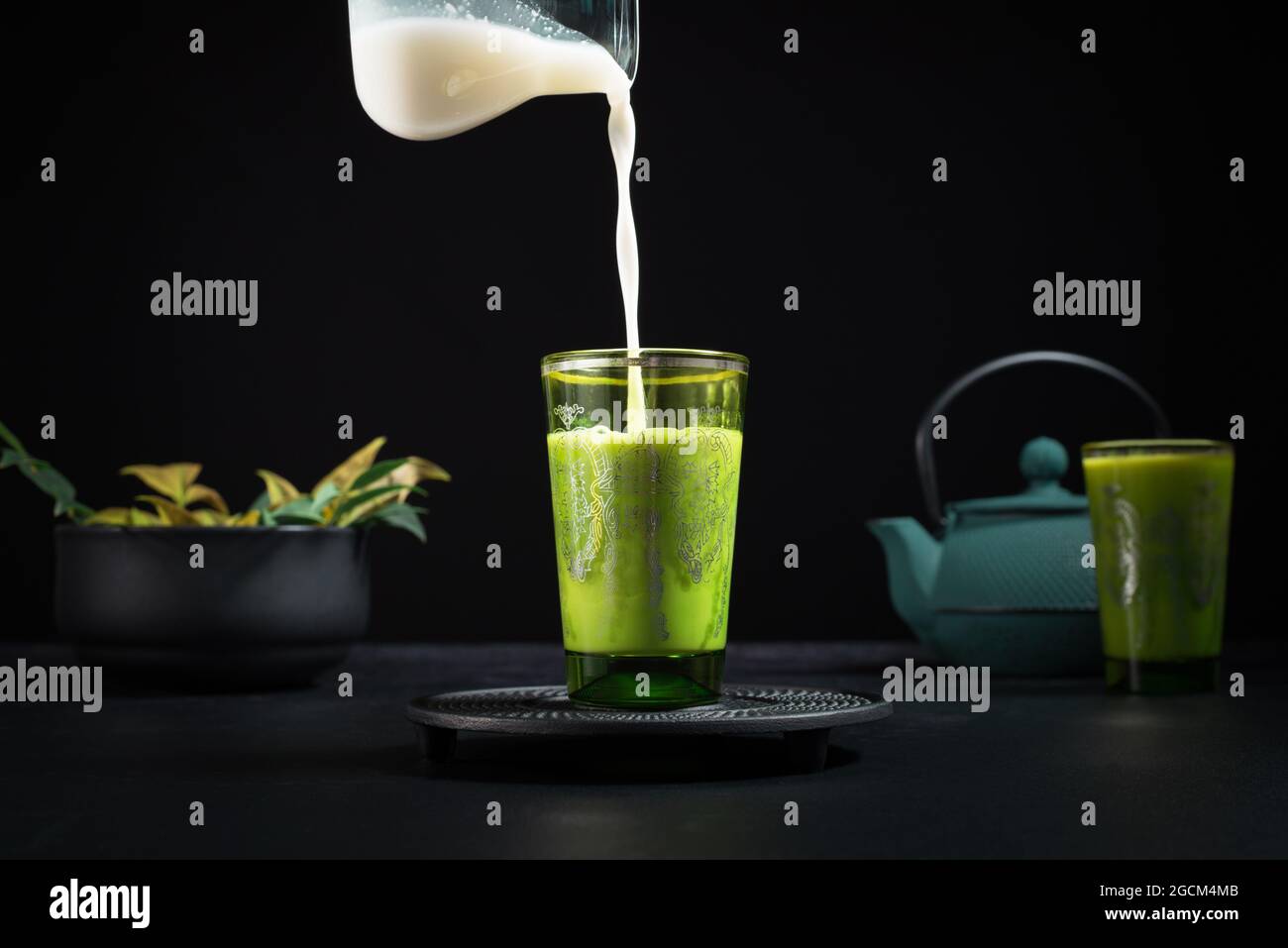 Il latte fresco viene versato dal vasetto in una tazza di vetro con il tè matcha posto sul tavolo con teiera e stoviglie durante la cerimonia tradizionale Foto Stock