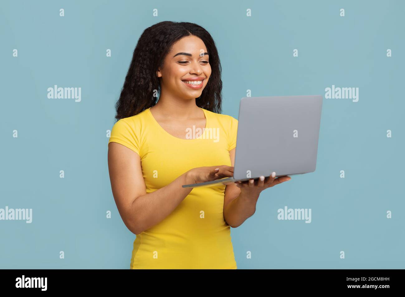 Programmi di formazione online. Donna nera felice che tiene e utilizza il computer portatile più recente su sfondo blu Foto Stock