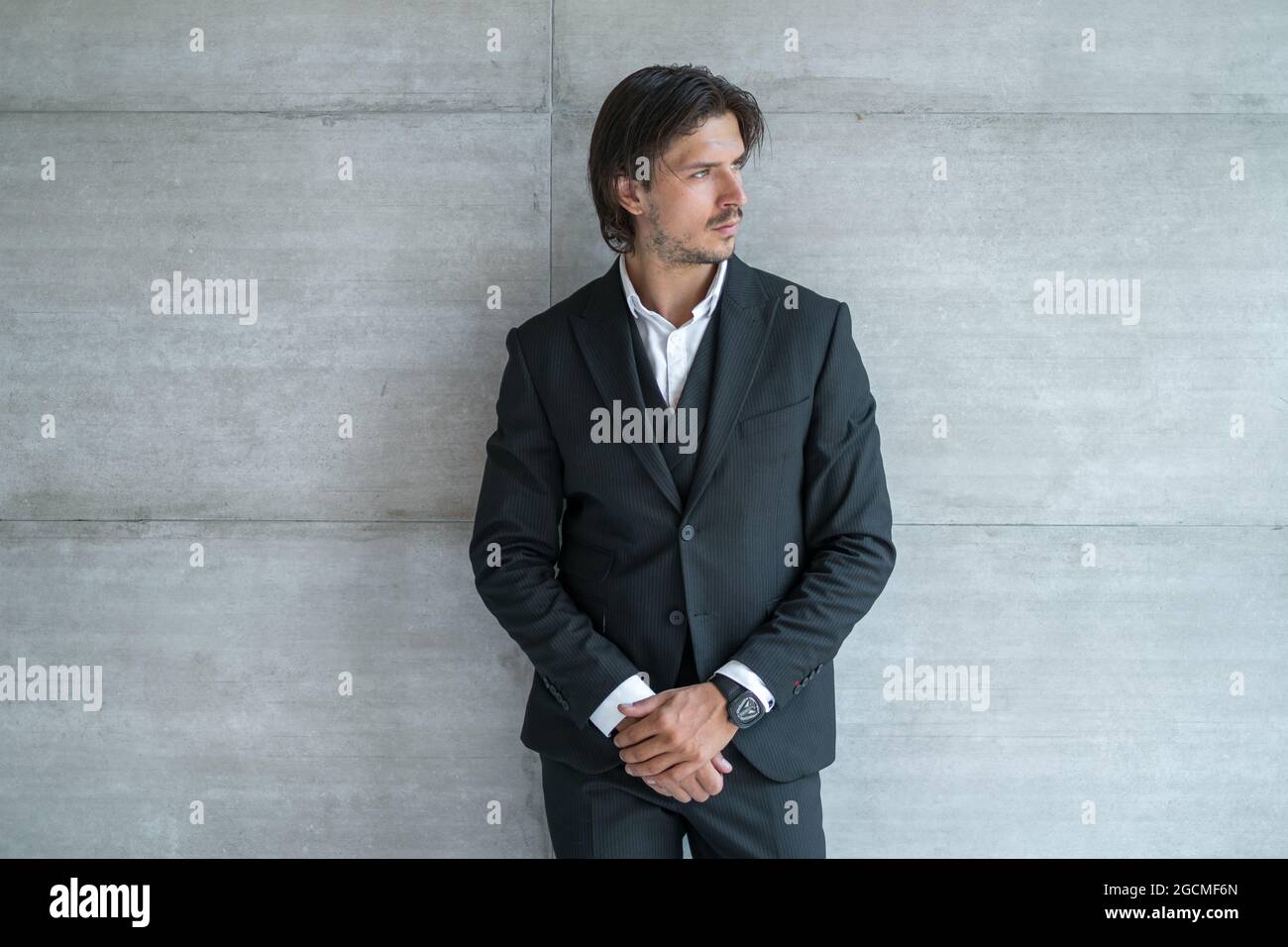 Elegante giovane uomo brunetto in tuta nera su sfondo grigio chiaro. Verticale. Foto di alta qualità Foto Stock