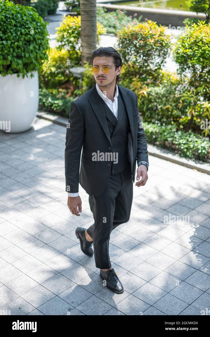 Uomo di successo in abito nero formale e occhiali da sole che cammina per strada e guardando da parte. Foto di alta qualità Foto Stock