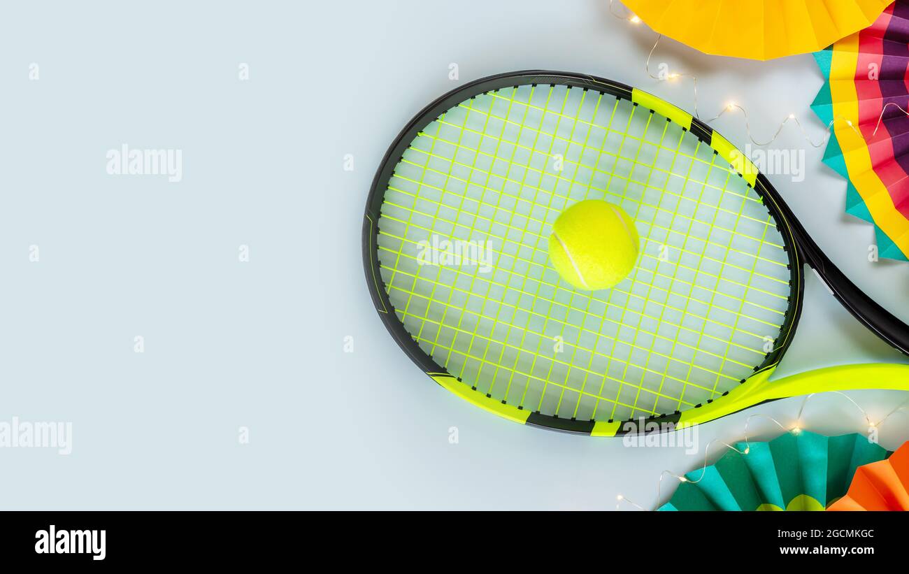 Tennis, composizione orizzontale con racchetta, palla da tennis gialla, ventilatori di carta colorati e un garland chiaro su sfondo blu con posto per il testo. Holi Foto Stock
