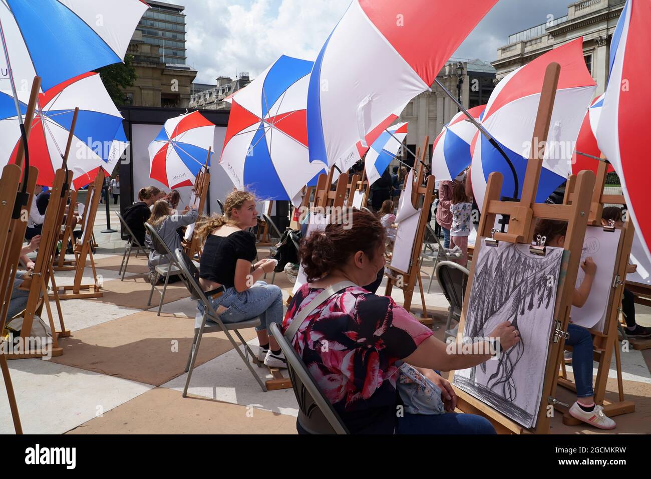 Londra, Regno Unito, 9 agosto 2021: La National Gallery offre lezioni d'arte in Trafalgar Square come parte del Festival Inside out per tutto il mese di agosto. Trenta cavalletti sono stati allestiti -- con ombrelli per il tempo estivo irregolare -- e persone di tutte le età possono cadere in Sketch sulla piazza per la guida nelle abilità di disegno. Anna Watson/Alamy Live News Foto Stock