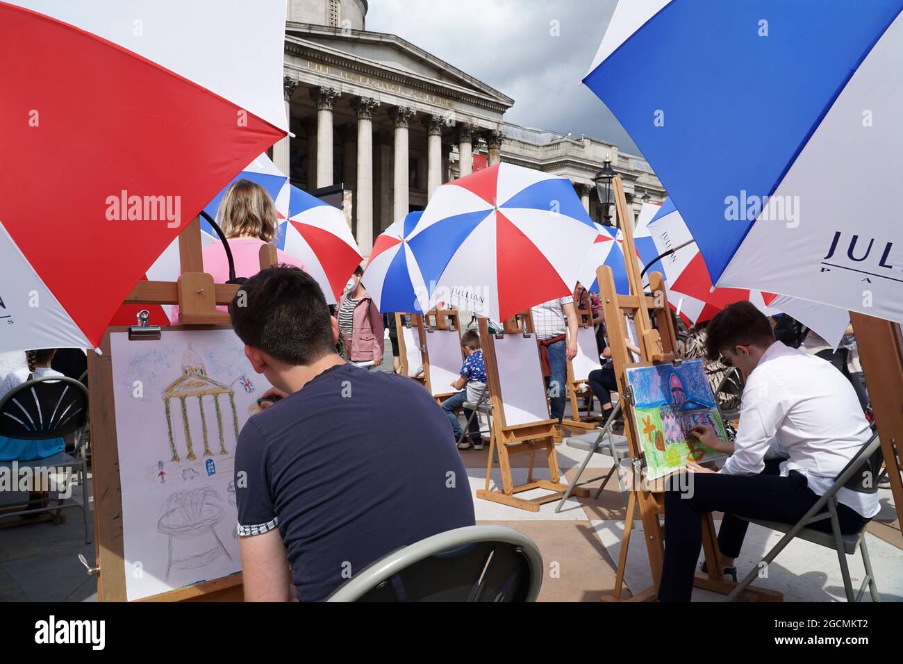 Londra, Regno Unito, 9 agosto 2021: La National Gallery offre lezioni d'arte in Trafalgar Square come parte del Festival Inside out per tutto il mese di agosto. Trenta cavalletti sono stati allestiti -- con ombrelli per il tempo estivo irregolare -- e persone di tutte le età possono cadere in Sketch sulla piazza per la guida nelle abilità di disegno. Anna Watson/Alamy Live News Foto Stock