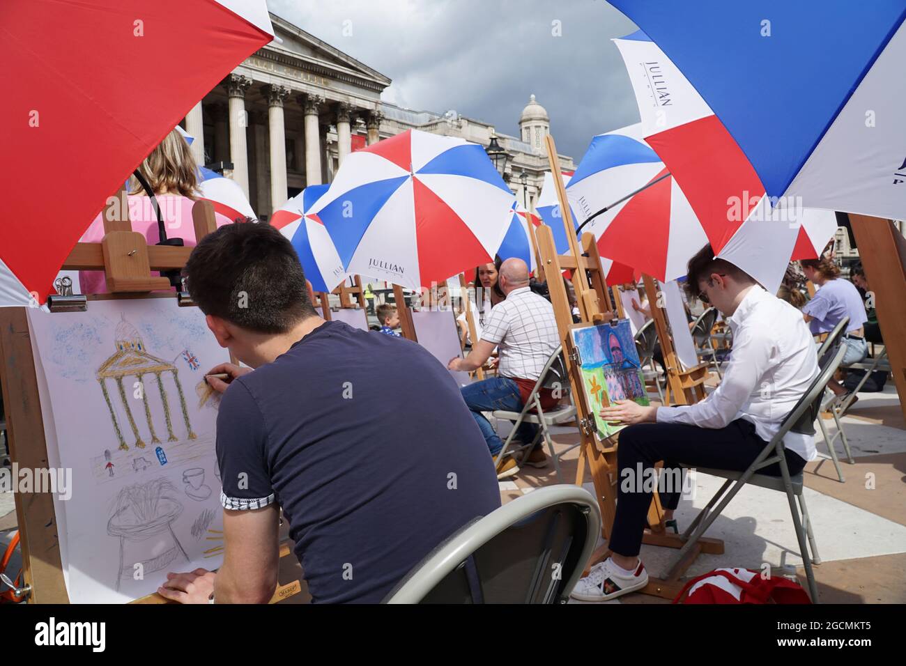 Londra, Regno Unito, 9 agosto 2021: La National Gallery offre lezioni d'arte in Trafalgar Square come parte del Festival Inside out per tutto il mese di agosto. Trenta cavalletti sono stati allestiti -- con ombrelli per il tempo estivo irregolare -- e persone di tutte le età possono cadere in Sketch sulla piazza per la guida nelle abilità di disegno. Anna Watson/Alamy Live News Foto Stock