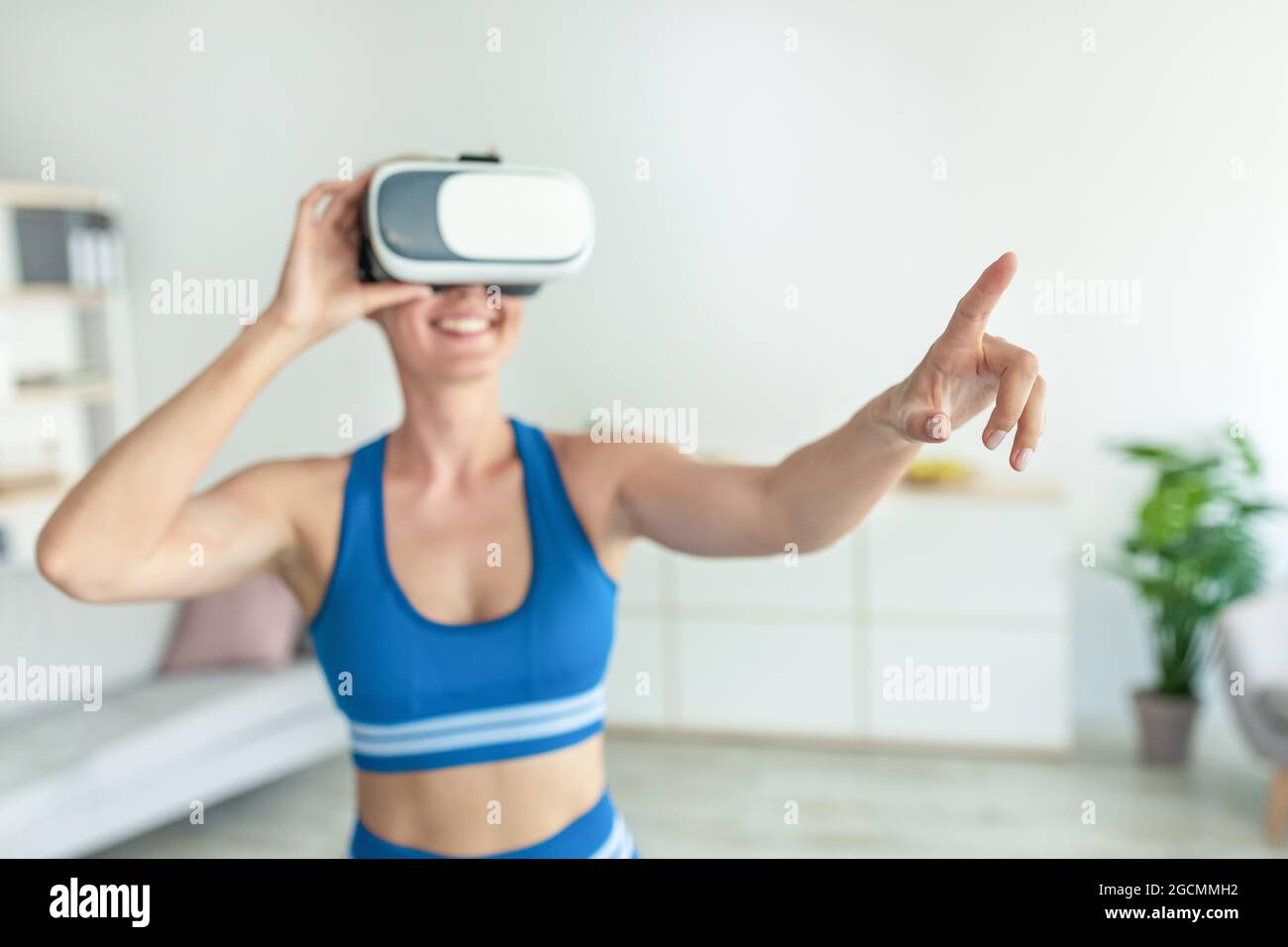 Donna sorridente con visore VR che si allena a casa Foto Stock