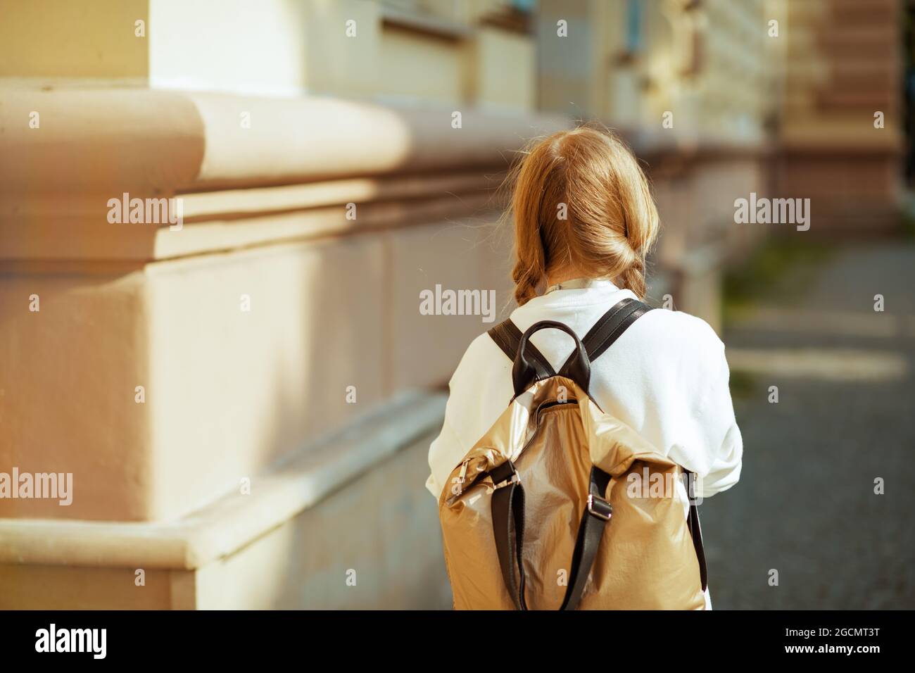 Visto da dietro allievo moderno in felpa bianca con zaino andare a scuola  all'aperto in città Foto stock - Alamy