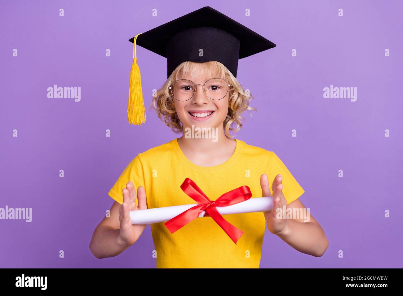 Foto di grazioso ragazzo scuola indossare occhiali giallo t-shirt graduazione livello elementare sorridente isolato colore viola sfondo Foto Stock